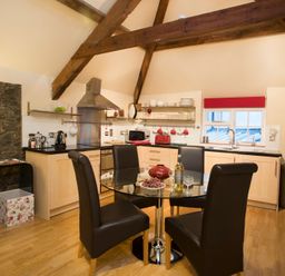 A kitchen with wooden beams glass dining table and black chairs at The Coach House in Beaumaris