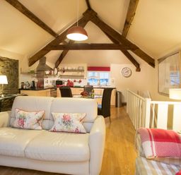 A living room and kitchen area with wooden beams and furniture at The Coach House - Beaumaris