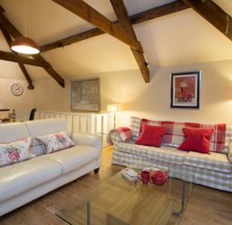 A living room with two sofas a glass coffee table and exposed wooden beams at The Coach House - Beaumaris