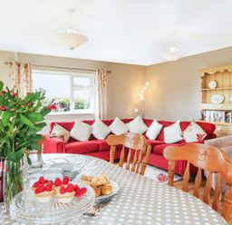 A dining table with flowers and pastries in a living room with a red sofa and wooden chairs at Coed Bolyn Lodge in Bethel