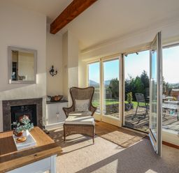 A living room with a fireplace wicker chair coffee table and glass doors opening to a patio at Cosy Barn in Llangaffo