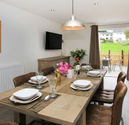A dining room with a wooden table set for six and leather chairs leading to a patio at Cuckooland in Borth-Y-Gest