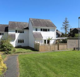 A white two-story house with a fenced patio and grassy yard under a clear blue sky at Cuckooland in Borth-Y-Gest