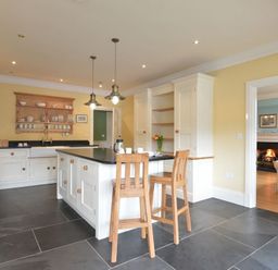 A kitchen with an island and two wooden chairs with a view into a living room with a fireplace at Dinas Noddfa in Nant Gwynant