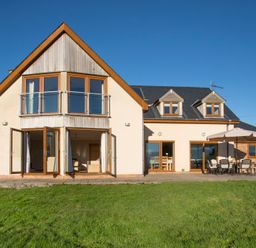 A modern house with large windows and doors opening to a patio with outdoor furniture and umbrella at Dol Fraint in Star