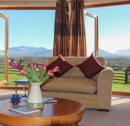 A living room with a wooden table holding a vase of flowers and books two armchairs with cushions and open doors revealing a rural landscape at Dol Fraint in Star