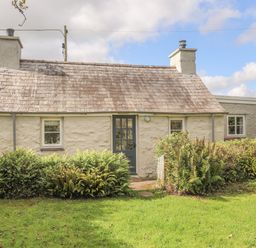 An exterior view of a small cottage with a tiled roof shrubs and grass in front at Ffrwd Cottage in Bodorgan
