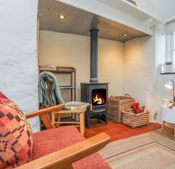 A sitting area with a wood burning stove two wicker baskets a red plaid pillow and a window at Ffrwd Cottage in Bodorgan
