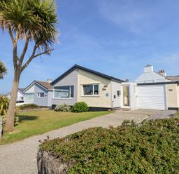 A single-story house with a driveway palm trees and a lawn near the coast at Flip Flops in Rhosneigr