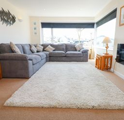 A living room with a grey sectional sofa a white rug wooden cabinet and side tables at Flip Flops in Rhosneigr