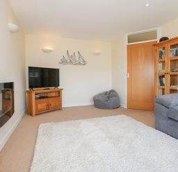 A living room with a television on a wooden stand a gray bean bag chair and a glass cabinet at Flip Flops in Rhosneigr