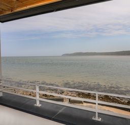 A view of the sea and shoreline from a balcony with a metal railing and roof at Four The Quay in Red Wharf Bay