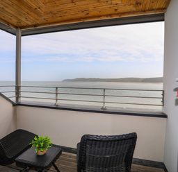 A balcony with two black wicker chairs and a table overlooking the sea at Four The Quay in Red Wharf Bay