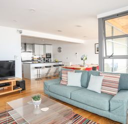 An open living space with a blue sofa beside a glass coffee table and a television on a wooden stand at Four The Quay in Red Wharf Bay