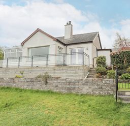 A house with a glass railing and concrete retaining walls surrounded by a grassy lawn at Frondeg in Rhiwlas