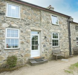 Stone house exterior with white windows wooden benches and a white door at Fron Fawr in Nefyn