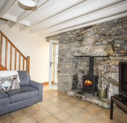 A living room with a gray sofa a stone fireplace with a wood burning stove and a television on a stand at Fron Fawr in Nefyn