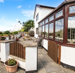 A patio area with wooden gates and a picnic table outside a white house with large windows at The Gables in Trearddur Bay