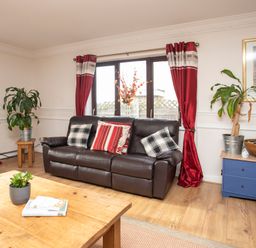 A living room with a leather sofa and red curtains at The Gables in Trearddur Bay