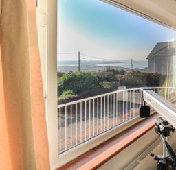 A window with beige curtains overlooking a garden and a distant view of water with a telescope on a tripod in the foreground at Garnedd Lwyd in Llanfair