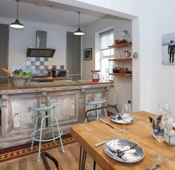 A kitchen with a wooden island and bar stools next to a dining table set with plates and glasses at Gwalia Stores in Beaumaris