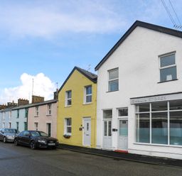 A street with parked cars and colorful row houses including Gwalia Stores in Beaumaris