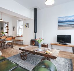 A living room with wooden coffee table, green leather sofas, TV on wooden stand, and dining table with chairs at Gwalia Stores in Beaumaris