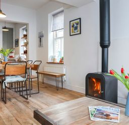 A dining area with wooden table and chairs next to a wood burning stove and a vase of tulips at Gwalia Stores in Beaumaris