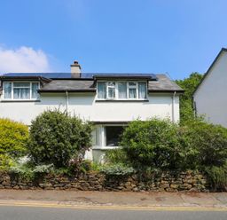 A two-story white house with solar panels on the roof and bushes in front at Gwyndy Bach in Beddgelert