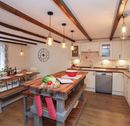 A kitchen with wooden dining table and benches and kitchen island with vegetables at Gwyndy Bach in Beddgelert