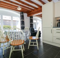 A dining area with a table and chairs next to a kitchen with cabinets and appliances at Hafod in Pontllyfni