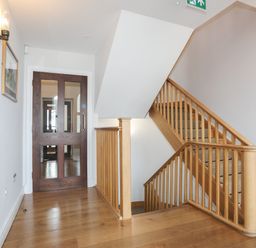 A staircase with wooden railings and carpeted steps next to a wooden door with glass panels at Harlech Apartments - Branwen in Harlech