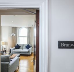 A living room with two grey sofas a wooden coffee table a floor lamp and a window at Harlech Apartments - Branwen in Harlech