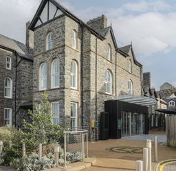 A stone building with multiple floors and arched windows with a modern glass entrance and surrounding plants at Harlech Apartments - Bendigeidfran Harlech