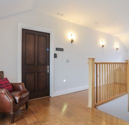 A hallway with a wooden door labeled Gwern a brown leather chair with a cushion and wooden railing at Harlech Apartments - Gwern Harlech