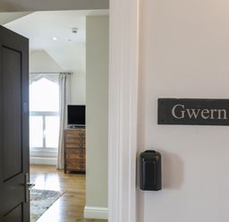 An open door showing a room with wooden flooring a chest of drawers a television and a window at Harlech Apartments - Gwern in Harlech