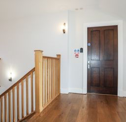 A hallway with wooden flooring a wooden staircase and a dark wooden door at Harlech Apartments - Matholwch in Harlech