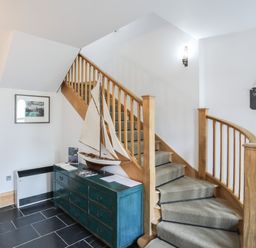 A staircase with wooden railing next to a blue chest of drawers with a model sailboat and a welcome sign on the white wall at Harlech Apartments - Matholwch in Harlech