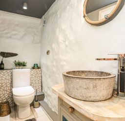 A bathroom with a toilet plants decorative items a round stone sink with a faucet and a wall mirror at Hen Gilfach in Llanfairyngnhornwy
