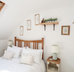 A bedroom with a wooden bed frame white bedding bedside tables lamps framed pictures and a wall shelf with plants at Hen Gilfach in Llanfairyngnhornwy