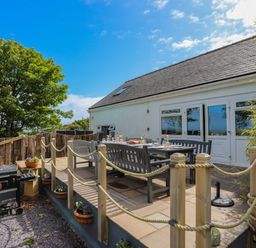 An outdoor patio with a dining table and benches next to a white building with a door and windows at Hen Gilfach in Llanfairyngnhornwy