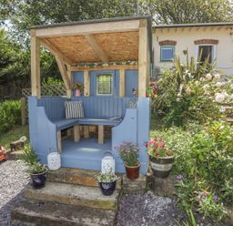 An outdoor wooden seating area painted blue with cushions and flower pots surrounded by plants and stone steps at Hen Gilfach Stable in Llanfairyngnhornwy