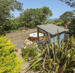 A garden with a hot tub next to a blue shed and various plants and trees at Hen Gilfach Stable in Llanfairyngnhornwy