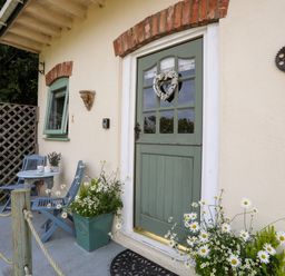 A porch with a green door and two blue chairs with a small table and flower pots at Hen Gilfach Stable in Llanfairyngnhornwy