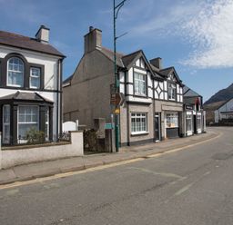 A street view with white and gray houses and a curved road with mountains in the background at Hirfron in Llanberis