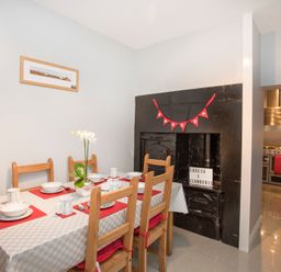 A dining area with a table set for six people and an old black fireplace with a red banner in a home at Hirfron in Llanberis