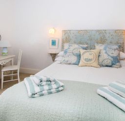 A bedroom with a bed with patterned pillows and folded towels a desk with a lamp and chair and two small framed pictures at Big House in Llandecwyn