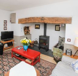 A living room with a wood stove under a wooden beam a red coffee table a television and patterned carpet at Big House in Llandecwyn