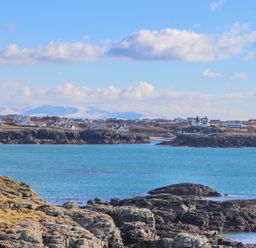 A coastal village with houses along rocky cliffs and blue water at Isallt in Trearddur Bay