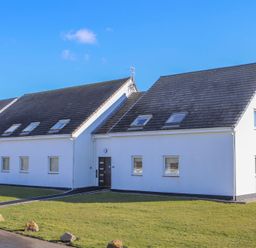 A white two-story residential building with multiple windows and skylights on a green lawn at Isallt in Trearddur Bay